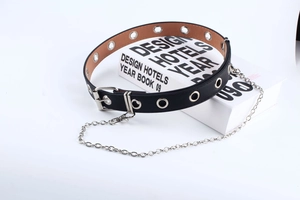 Nahaufnahme vom schwarzen Punk Gürtel mit silbernen Ösen und Kette auf weißem Buch