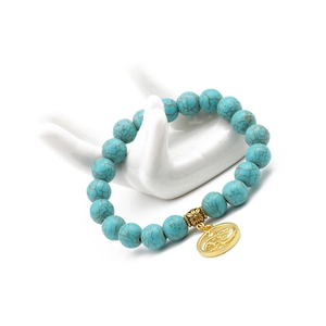 Detail of 10mm turquoise beaded bracelet with golden Om charm on a white display