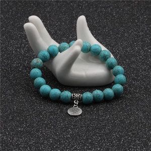 Detail of 10mm turquoise beads with a silver tree of life charm on a ceramic hand display