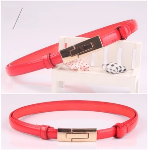 Detail of slim red patent leather belt for women featuring a sleek gold metal buckle