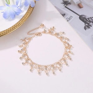 Close-up of golden metal anklet with sparkling rhinestone tassels on white background