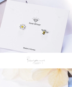 Detail of asymmetric 925 silver studs with white daisy flower and yellow bee charms