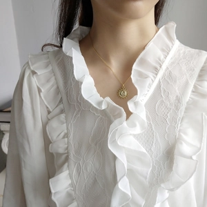 Detail of a vintage sun pendant necklace in gold finish on a model wearing white lace