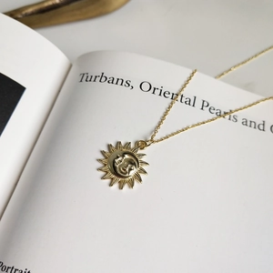 Close-up of a gold smiling sun pendant necklace displayed on a white open book page