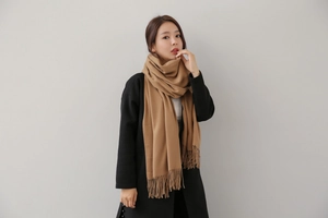 Close-up of camel cashmere scarf texture and detailed twisted tassels with black coat