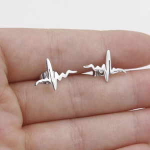 Detailed view of silver stainless steel heartbeat stud earrings held to show scale