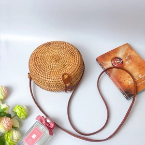 Handmade round rattan bag with leather strap and snap closure in a lifestyle setting
