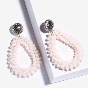 Detail van handgemaakte boho-oorbellen met crème kralen en pavé-gezette strasstenen