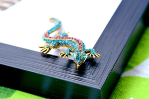 Close-up of vibrant gecko brooch with blue, pink and green crystals on a black frame