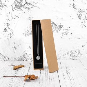 Detail of silver chain necklace with round jade pendant in long kraft paper jewelry box