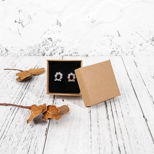 Close-up of floral stud earrings in silver and rose gold inside a kraft paper jewelry box