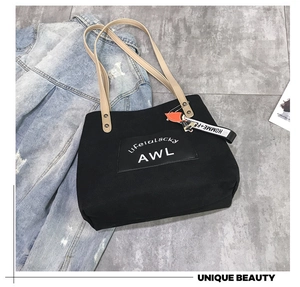 Detail of black canvas tote bag with contrast cream straps and red doll pendant accessory