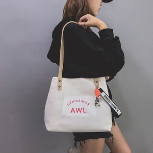 Close-up of white canvas tote bag with leather straps and red lettering on model
