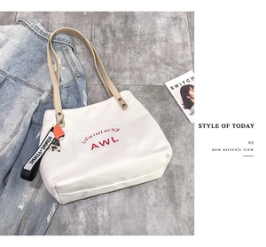 Close-up of a white canvas tote bag with brown straps and a black logo ribbon charm