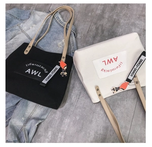 Detail of canvas tote bags in black and white with leather straps and cartoon charms