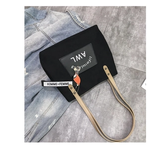 Close-up of black canvas tote bag with lettered straps and patches on marble floor