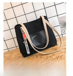 Detail of black canvas tote bag with beige leather handles and stylish lettered pendant