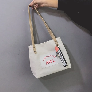 Detail of white canvas tote bag featuring red AWL print and decorative charm on handle