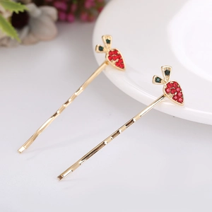 Macro detail of two golden carrot hair pins decorated with red and green rhinestones