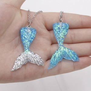 Detail shot of two gradient blue and silver glitter resin mermaid tail pendants on chains