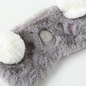 Close-up of soft grey and white plush sleep mask with detailed embroidery and texture