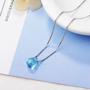 Minimalist silver necklace with light blue teardrop crystal pendant on white background