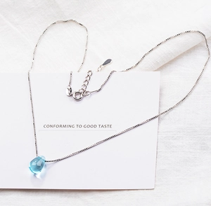 Macro detail of a 925 sterling silver box chain with a teardrop blue crystal pendant