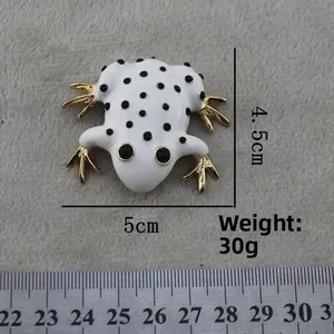 Detailed size view of a white enamel frog brooch with black dots and golden metal limbs