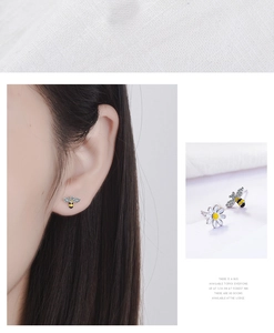 Detail of asymmetric daisy and bee stud earrings featuring enamel and white cubic zirconia