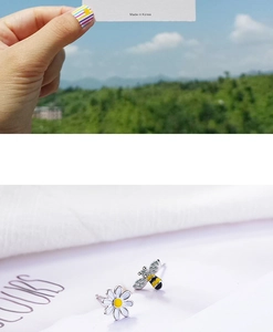 Detail of asymmetric daisy and bee earrings with silver petals and yellow enamel finish