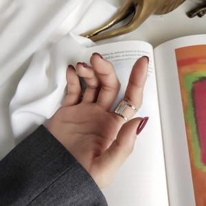 Macro shot of silver wide geometric cutout open ring worn against white silk and books