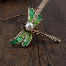 Detail of a dragonfly brooch with green enamel wings and a pearl on a rustic wood surface