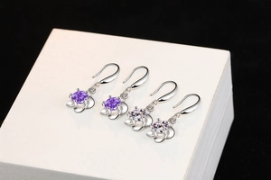 Detailed close-up of floral silver earrings with purple and clear zircon stones in a box