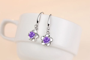 Macro detail of silver plum blossom earrings with purple zircon on a ceramic cup