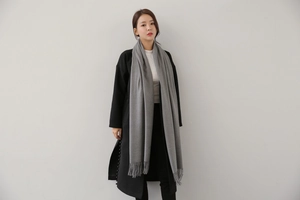 Close-up of grey solid cashmere scarf with fringe details worn over a black winter coat