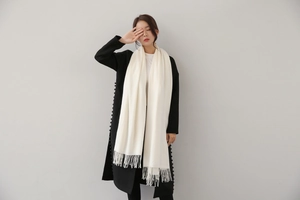 Close-up of off-white cashmere scarf with long tassels paired with a black wool coat