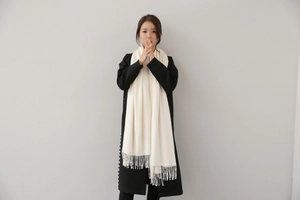Detail of cream white cashmere scarf with long fringe tassels paired with a black coat