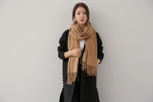 Detail of camel cashmere-feel scarf with tassels worn by model over a black coat
