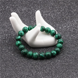 Detailed macro view of 10mm malachite stone beads on white ceramic hand display