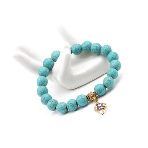 Detail of turquoise bead bracelet with gold Hamsa Hand and Evil Eye charm on white model