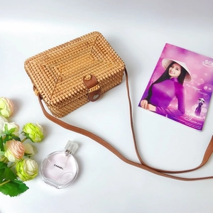 Detail view of a woven rattan crossbody bag with brown leather strap and closure