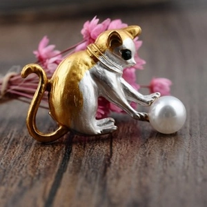 Detailed close-up of a two-tone gold and silver cat brooch playing with a large pearl