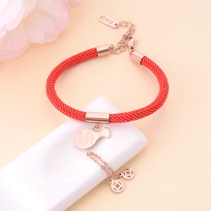Detail of rose gold money bag and coin charms on a red woven lucky cord bracelet