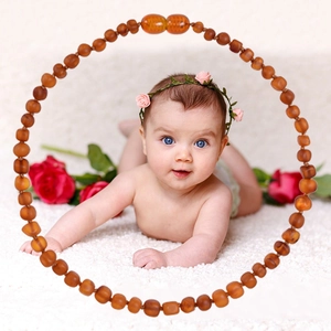Natural Baltic amber baby necklace for infants on white plush rug with red roses
