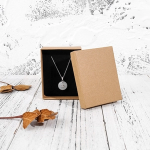 Close-up of a circular stone pendant in a brown kraft jewelry gift box with dry leaf decor