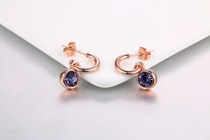 Detailed view of gold plated earrings with round purple zircon pendants on white ceramic