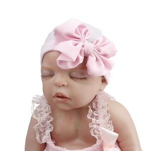 Detail of white newborn baby knit hat with large pink satin bow on model