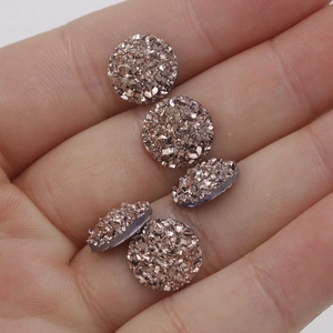 Close-up of 10mm rose gold resin druzy cabochons with sparkling starry surface texture