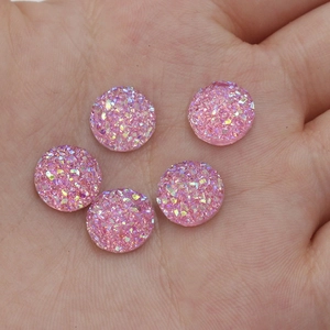 Detailed view of 10mm pink resin druzy cabochons held in hand for size comparison