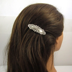 Vintage zilveren metalen haarclip met bloemenreliëf op bruin haar, zijaanzicht van opzij